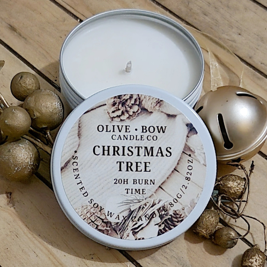 Olive Bow Candle Co Christmas Tree scented soy candle in a tin on a wooden surface with decorative elements.